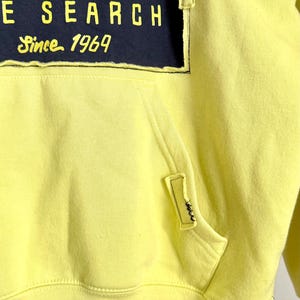 May include: A yellow hoodie with a front pocket and a drawstring hood. The hoodie features a large graphic on the front with the text "PCURL", "E SEARCH", and "Since 1969" in yellow and white on a navy blue background.