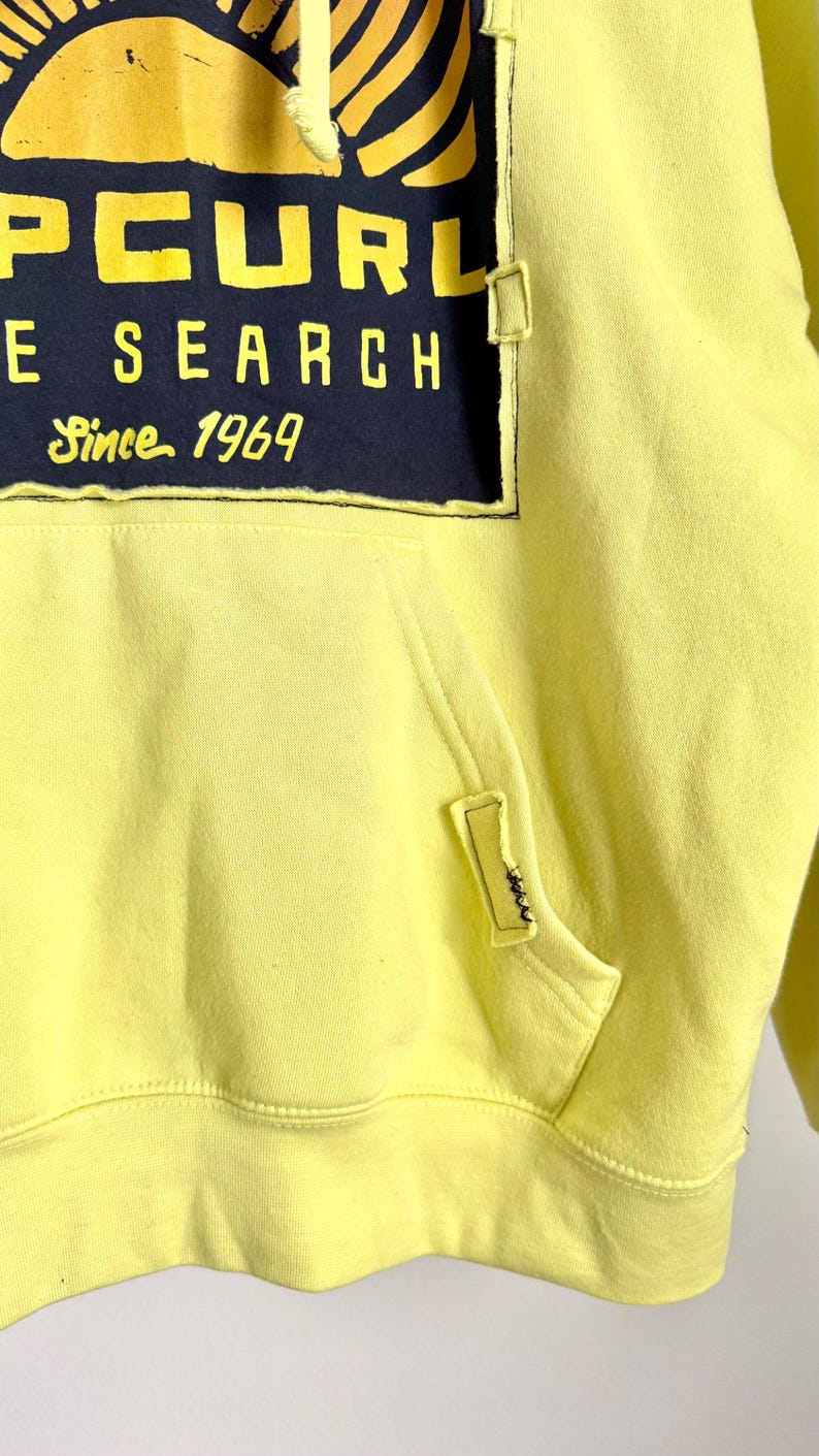 May include: A yellow hoodie with a front pocket and a drawstring hood. The hoodie features a large graphic on the front with the text "PCURL", "E SEARCH", and "Since 1969" in yellow and white on a navy blue background.