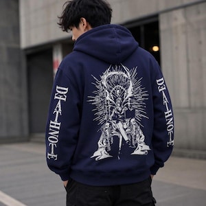 May include: A dark navy blue hooded sweatshirt featuring a large white graphic print on the back depicting a figure sitting on a throne with a scythe and skulls. The text DEATH NOTE is printed vertically in white on both sleeves of the garment.