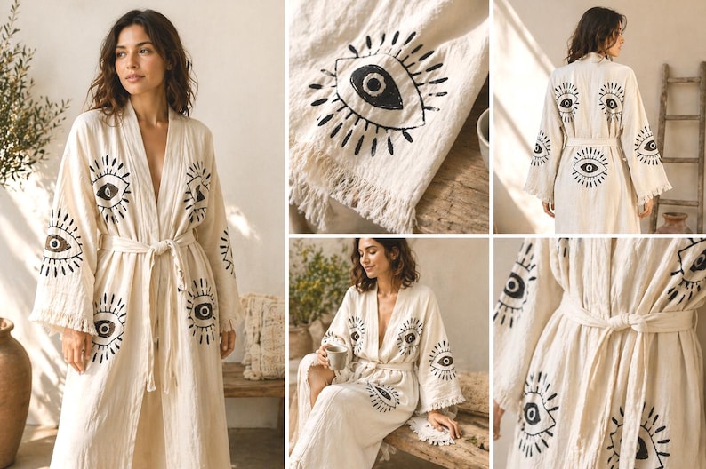 May include: Cream-colored robe with a repeating black eye design. The robe has long sleeves, a tie waist, and a flowing silhouette. The eye motif is printed on the front, sleeves, and back. The fabric appears to be lightweight and textured, suitable for lounging.