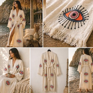 May include: Cream-colored robe with an embroidered eye design in red, orange, and black. The robe has long sleeves, a belt, and fringe detailing. The eye motif is repeated on the sleeves and front of the robe. The robe is made of a soft, flowing fabric.