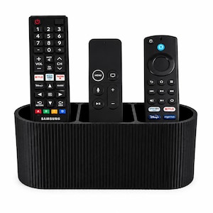 May include: A black, oval-shaped remote control holder with a vertical ribbed texture. The organizer features three distinct compartments, each currently holding a different black remote control for electronic devices.