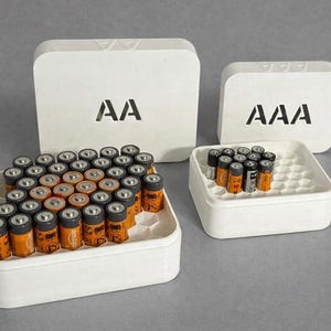 May include: White battery organizers with AA and AAA labels. The AA organizer holds numerous orange and black batteries. The AAA organizer holds a smaller quantity of batteries. The organizers are on a gray surface.
