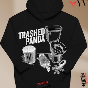 May include: Black hoodie with a white graphic design. The design includes the text "Trashed Panda", a toilet, a raccoon, a trash can, and a spilled bottle. A humorous illustration.
