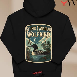 May include: Black hooded sweatshirt featuring a graphic of a loon on water with the text "STUPID CANADIAN WOLFBIRD". The design includes a crescent moon, cattails, and pine branches. The sweatshirt has a drawstring hood and a kangaroo pocket.