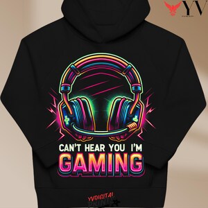 Pode incluir: Moletom preto com um gráfico de fones de ouvido neon e o texto "CAN'T HEAR YOU I'M GAMING". O design usa rosa, azul, verde e amarelo. O moletom tem capuz com cordão e um bolso frontal.