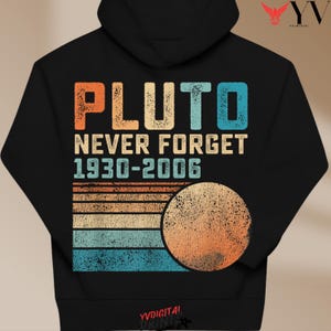 May include: A black hooded sweatshirt featuring a graphic print with the text PLUTO NEVER FORGET 1930-2006. The design includes a distressed, multi-colored horizontal striped pattern in orange, beige, and blue, alongside a circular planet graphic.