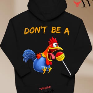 Könnte beinhalten: Schwarzer Kapuzenpullover mit dem Text "DON'T BE A" in Orange. Die Grafik zeigt einen Cartoon-Hahn mit rotem Kamm, gelbem Schnabel und blauem Körper, der einen Lolli hält.