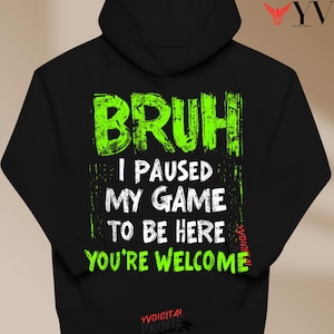 May include: Black hoodie with the text "BRUH I PAUSED MY GAME TO BE HERE YOU'RE WELCOME" in neon green and white. The hoodie has a drawstring hood and a kangaroo pocket. The design is centered on the front.