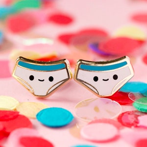 May include: A pair of gold-toned earrings with a white and blue enamel design of a smiling pair of underwear.