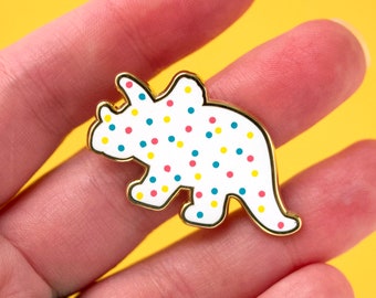 May include: Gold-tone enamel pin shaped like a white triceratops with red, yellow, and blue polka dots.