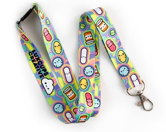 May include: A colorful lanyard with a rainbow tie-dye pattern and a repeating pattern of cartoon pills, bandages, and clouds. The lanyard has a black clip and a silver swivel hook. The text "LUXCUPS CREATIVE" is printed on the lanyard.