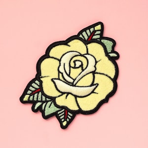 May include: A yellow embroidered rose with black outlines and green leaves on a pink background.