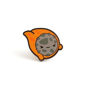 May include: Orange and gray enamel pin of a cartoon rock with a smiling face. The rock is in a curled up position, as if it is rolling.
