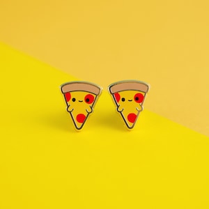 May include: A pair of gold-colored earrings shaped like pizza slices with red pepperoni and a smiling face.