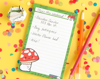 May include: A green and white notepad with a mushroom illustration and the text "Plans this weekend!"  The notepad has a lined interior and the text "Garden Center 323 Elm st.  Buy potting mix Water flower bed Nap!" is written on the notepad.