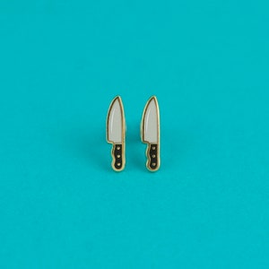 May include: A pair of gold-toned earrings shaped like knives with white blades and black handles.