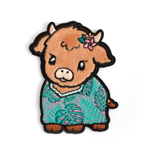 May include: Embroidered patch of a brown cow wearing a green and pink floral dress. The cow has a pink flower on its head.