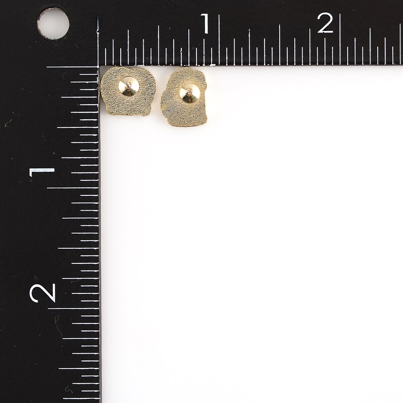 May include: Two gold-toned earrings with a textured, irregular shape. Each earring has a small, round, gold-toned stud in the center.
