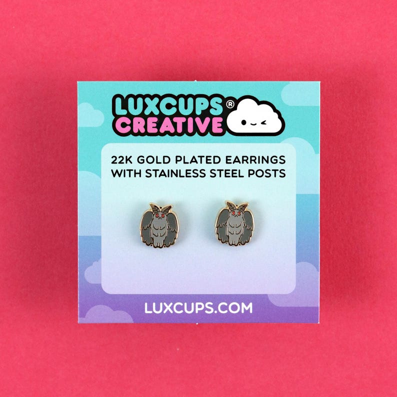 K&ouml;nnte beinhalten: Zwei goldbeschichtete Ohrringe mit Edelstahlstiften, die ein graues Motten-Design zeigen. Sie sind auf einer t&uuml;rkis-wei&szlig;en Karte mit dem Text "LUXCUPS CREATIVE" und "LUXCUPS.COM" abgebildet. Der Hintergrund ist pink.