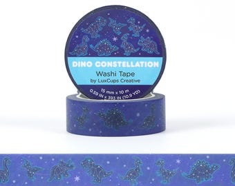 以下が含まれることがあります： Dino Constellationのマスキングテープのロール。テープは濃い青色で、恐竜の星座の繰り返し模様があります。ラベルには「Dino Constellation Washi Tape by LuxCups Creative」と書かれています。テープの幅は1.5cm、長さは10mです。