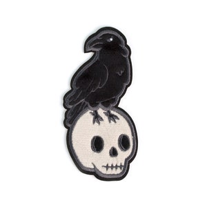 May include: Black crow perched on a white skull with black eye sockets. The crow and skull are embroidered on a fabric patch.