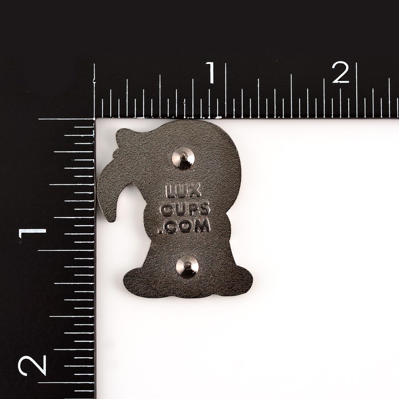 May include: A dark gray enamel pin with a stylized bird design. The pin has two metal clasps on the back and the text "LUX CUPS .COM". The pin is approximately 1 inch in height.