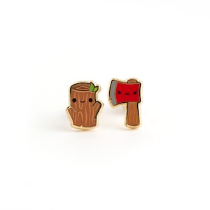 May include: A pair of gold-tone earrings featuring a smiling tree stump and a frowning axe. The tree stump is brown with a green leaf on top. The axe is red with a gray handle.