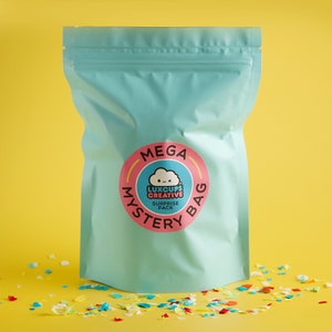 May include: A teal blue zippered pouch with a pink circle sticker that says "MEGA MYSTERY BAG" with a white cloud and the text "LUXCUPS CREATIVE SURPRISE PACK" inside the circle.