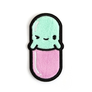May include: A green and pink plush pill shaped patch with a cartoon face. The pill has a winking eye and a small smile.