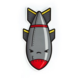 May include: A gray cartoon bomb sticker with a red nose cone and a red stripe. The bomb has yellow accents on the fins and a grumpy face. The sticker has the text "LUXCUBE.COM" on the fins.