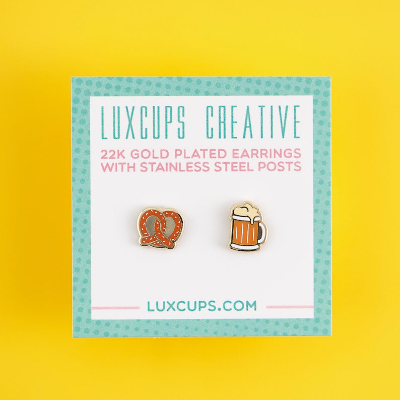May include: A pair of gold-plated earrings featuring a pretzel and a beer mug. The earrings are on a white card with the text "LUXCUPS CREATIVE 22K GOLD PLATED EARRINGS WITH STAINLESS STEEL POSTS LUXCUPS.COM".