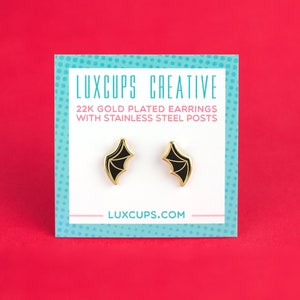 May include: A white card with black text that reads "Luxcups Creative" and "22K Gold Plated Earrings with Stainless Steel Posts". The card also has the website "luxcups.com" printed on it. Two gold earrings with black bat wings are displayed on the card.