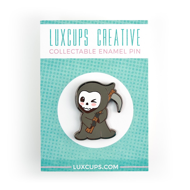 May include: A collectible enamel pin featuring a cartoon Grim Reaper character with a winking eye and a scythe. The pin is gray, brown, and white, with the text "LUXCUPS CREATIVE" and "COLLECTABLE ENAMEL PIN" on the backing card. The website address is also visible.