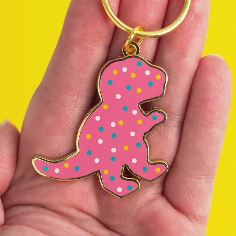 May include: A pink dinosaur-shaped keyring with a gold ring and colourful sprinkles.