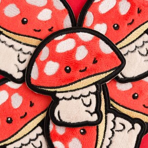 May include: A set of six red and white felt mushroom patches with embroidered details. Each mushroom has a smiling face and white spots.
