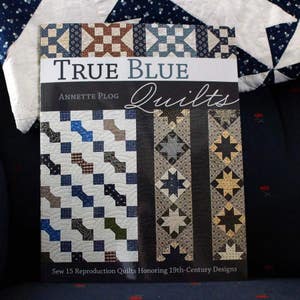 May include: Book cover featuring a blue and white quilt pattern with the title "True Blue Quilts" by Annette Plog. The book cover also includes the text "Sew 15 Reproduction Quilts Honoring 19th-Century Designs".