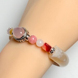 Pu&ograve; includere: Un braccialetto di perline con una grande gemma rosa, perline rosa e bianche pi&ugrave; piccole e una grande pietra colorata chiara. Il braccialetto ha dettagli in metallo color argento.