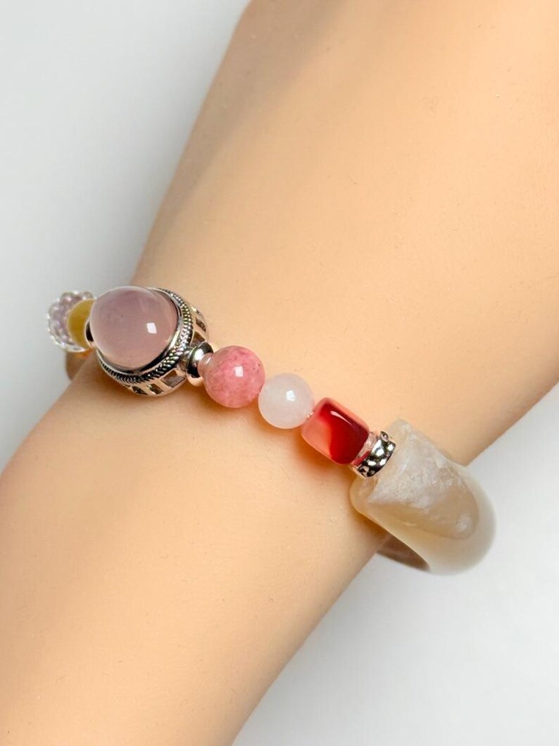 Pu&ograve; includere: Un braccialetto di perline con una grande gemma rosa, perline rosa e bianche pi&ugrave; piccole e una grande pietra colorata chiara. Il braccialetto ha dettagli in metallo color argento.
