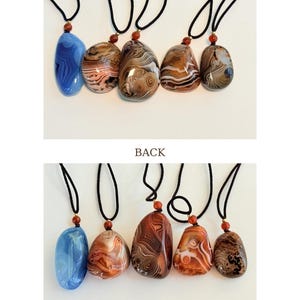 May include: A collection of six gemstone pendants with black cords. The pendants display a variety of colors and patterns, including blue, brown, and orange. Each pendant is unique. The text reads: "Each pendant is one of a kind. Natural patterns and colors will vary."