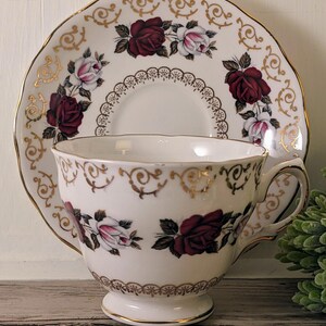 Puede incluir: Juego de taza y platillo blancos con dise&ntilde;o de rosas burdeos y rosas. El platillo tiene un borde festoneado. La taza y el platillo est&aacute;n decorados con detalles dorados.