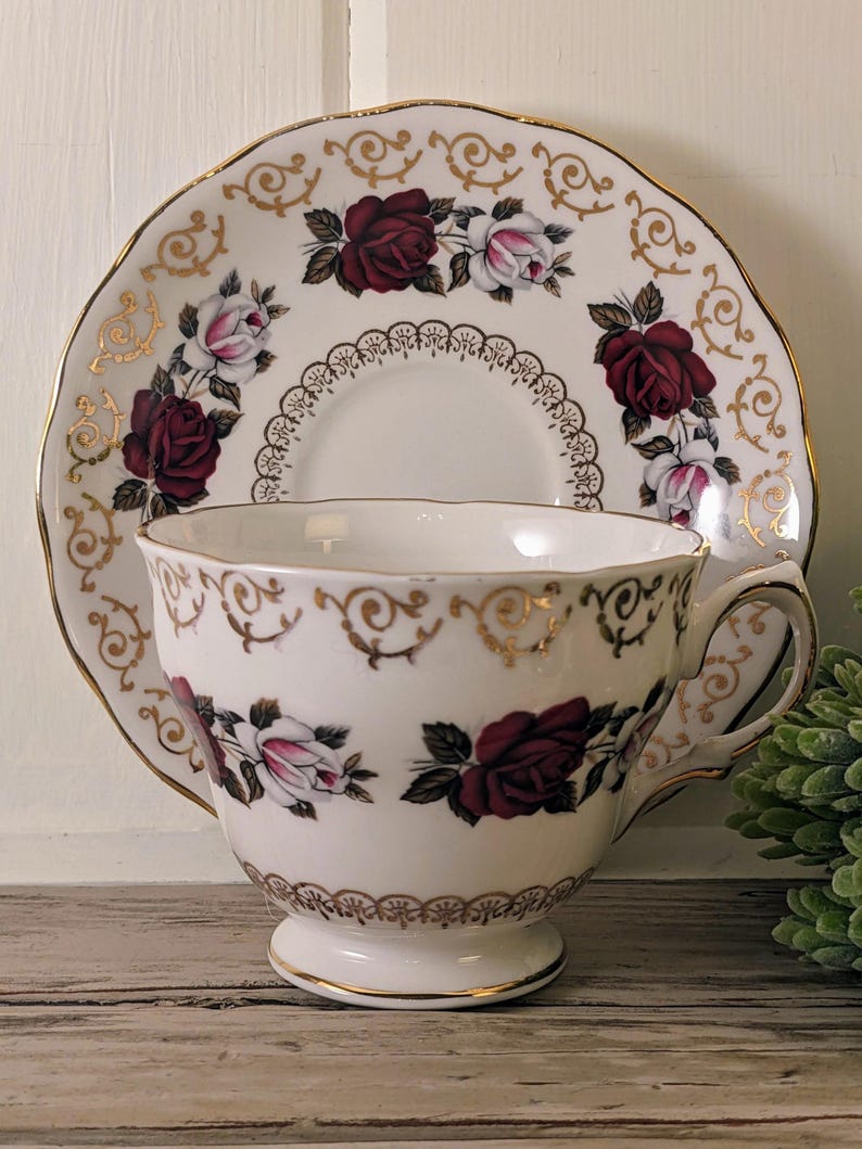 Puede incluir: Juego de taza y platillo blancos con dise&ntilde;o de rosas burdeos y rosas. El platillo tiene un borde festoneado. La taza y el platillo est&aacute;n decorados con detalles dorados.