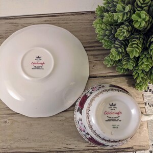 Puede incluir: Un juego de taza y platillo Colclough blanco con un dise&ntilde;o floral de rosas rojas y flores rosas. El platillo tiene un borde festoneado. El nombre de la marca Colclough es visible en la taza y el platillo.