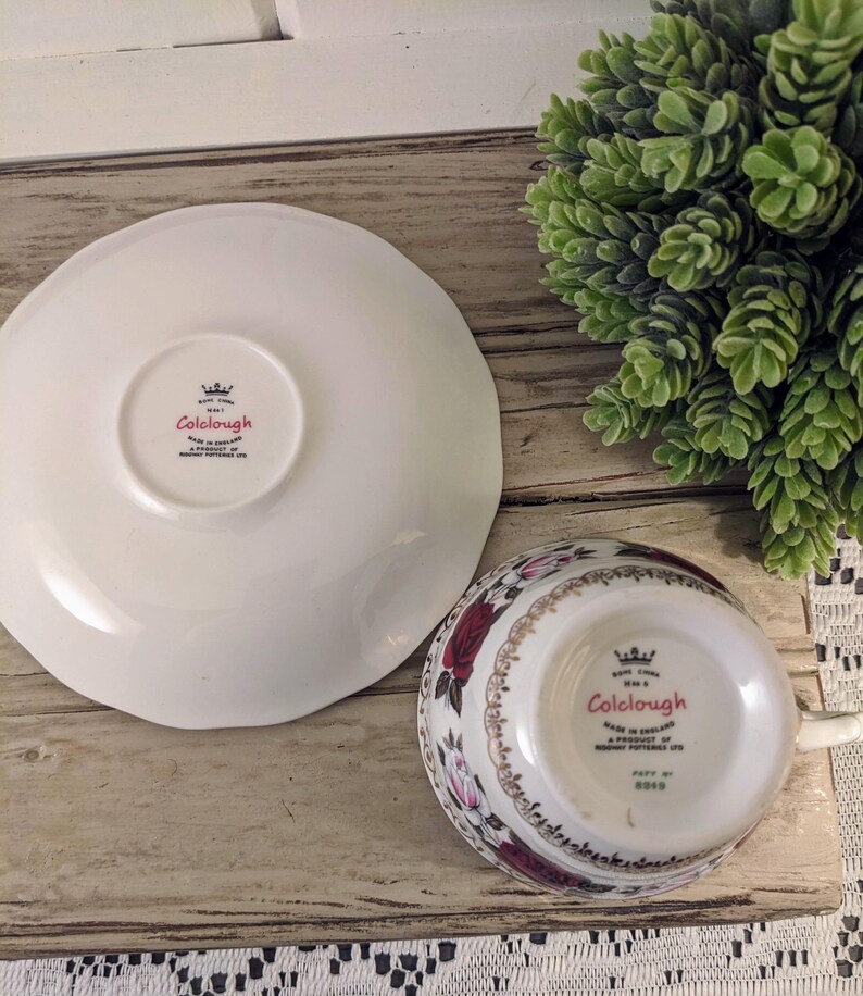 Puede incluir: Un juego de taza y platillo Colclough blanco con un dise&ntilde;o floral de rosas rojas y flores rosas. El platillo tiene un borde festoneado. El nombre de la marca Colclough es visible en la taza y el platillo.