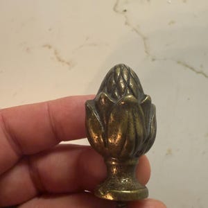 May include: A bronze cabinet knob with a floral design. The knob has a detailed, textured surface and a screw for attachment. The design resembles a stylized flower or artichoke, adding a touch of vintage charm to furniture.