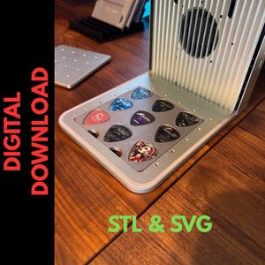 Puede incluir: Un soporte plateado para púas de guitarra con nueve púas de varios colores y diseños. El soporte está sobre una superficie de madera. El texto "DIGITAL DOWNLOAD" está en el lado izquierdo de la imagen y "STL & SVG" en la parte inferior.