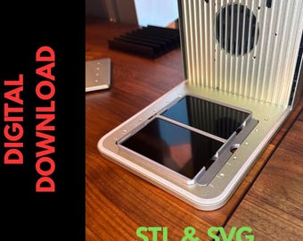 May include: A silver-colored, rectangular device with a slot for a tablet or phone, featuring a ribbed back and a circular opening. The words "DIGITAL DOWNLOAD" are in red text on a black background. The text "STL & SVG" is in green.