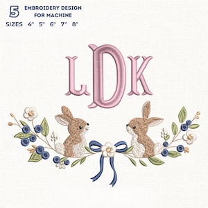 Könnte beinhalten: Stickdesign für Maschinen mit den Buchstaben LDK in Rosa, über zwei braunen Hasen. Die Hasen sind von einem Kranz aus Blaubeeren, Blättern und weißen Blumen mit einer blauen Schleife umgeben. Text: "EMBROIDERY DESIGN FOR MACHINE" und "GRÖSSEN 10cm 13cm 15cm 18cm 20cm".