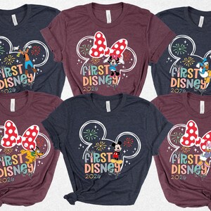 May include: A collection of six short-sleeved t-shirts. Each shirt features a colorful graphic with the text "First Disney 2020" and a Mickey Mouse head design. The shirts are in various colors, including navy blue and burgundy.