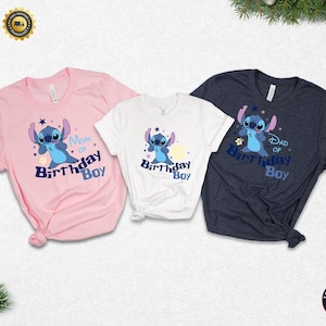 K&ouml;nnte beinhalten: Drei kurz&auml;rmelige T-Shirts mit einem Cartoon-Charakter-Design. Die Shirts sind rosa, wei&szlig; und marineblau. Jedes Shirt zeigt eine blaue Cartoon-Figur mit dem Text "Mom of Birthday Boy", "Birthday Boy" und "Dad of Birthday Boy".